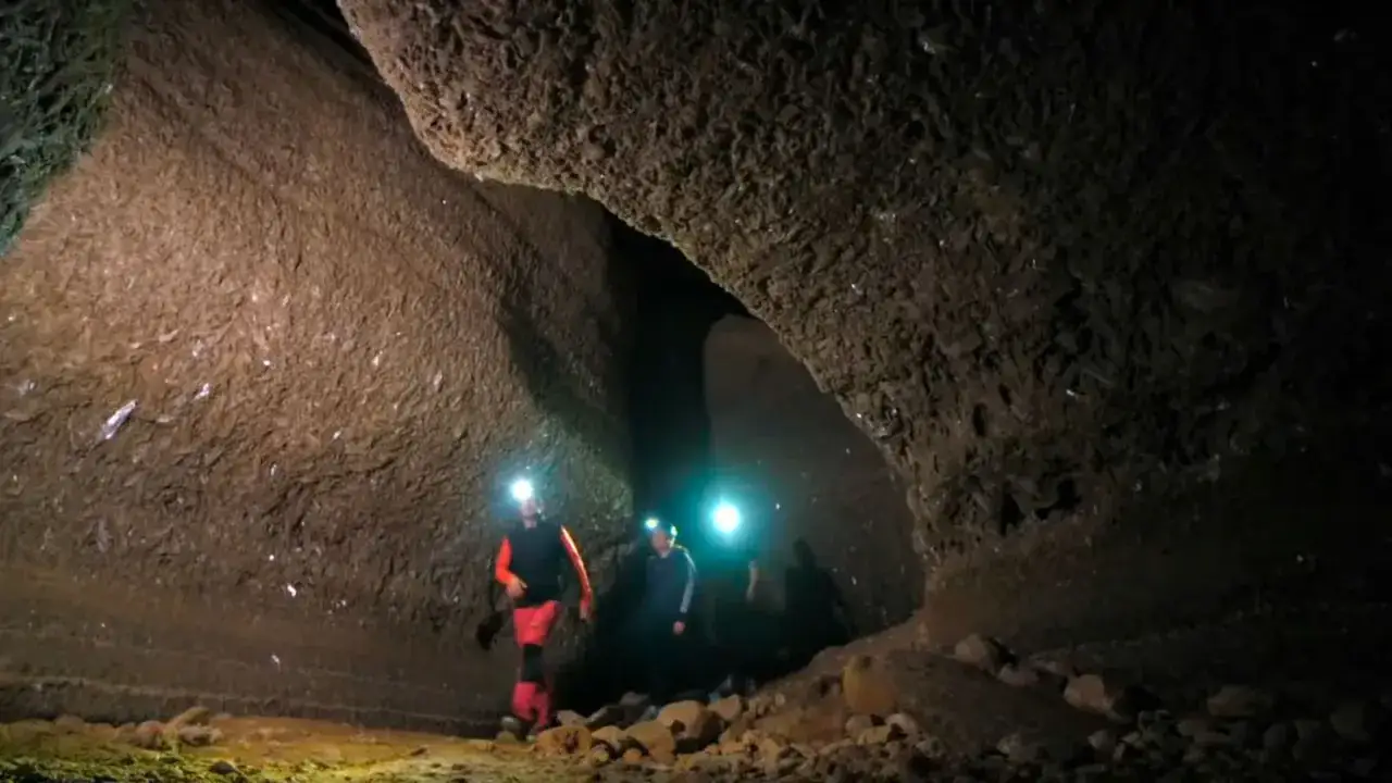 Exploradores con linternas iluminan las paredes de una cueva, revelando formaciones de **los yesos** que brillan en la oscuridad.