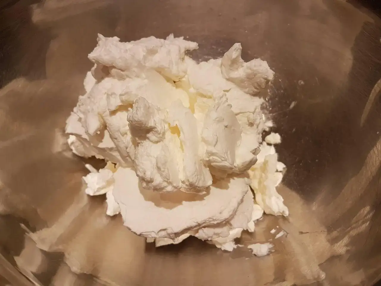 Puszysta bita śmietana z mascarpone w metalowej misce, gotowa do deseru.