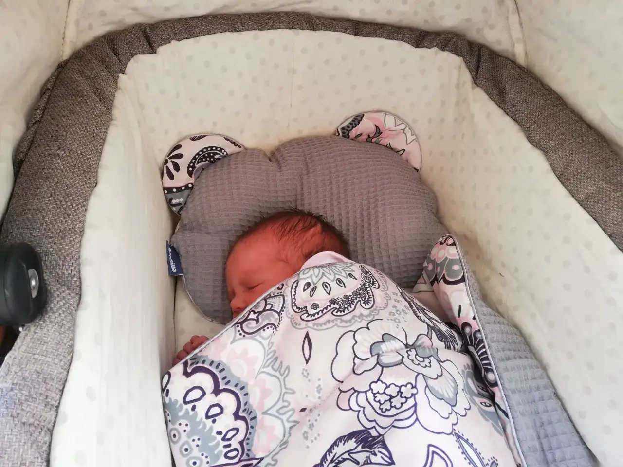 Słodki noworodek śpi w wózku, otulony kolorowym kocykiem. Idealny moment na pierwszy spacer z noworodkiem.