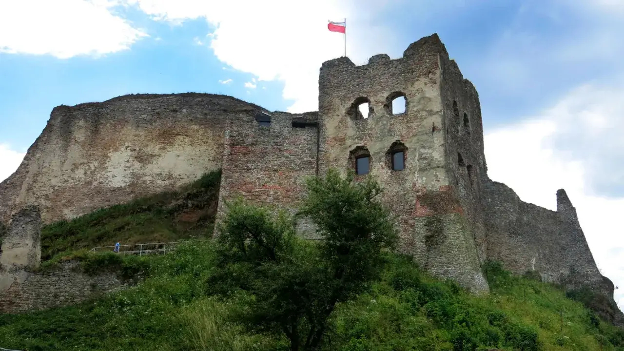 Ruiny zamku w Zakopanem, z polską flagą na wieży, otoczone zielenią.