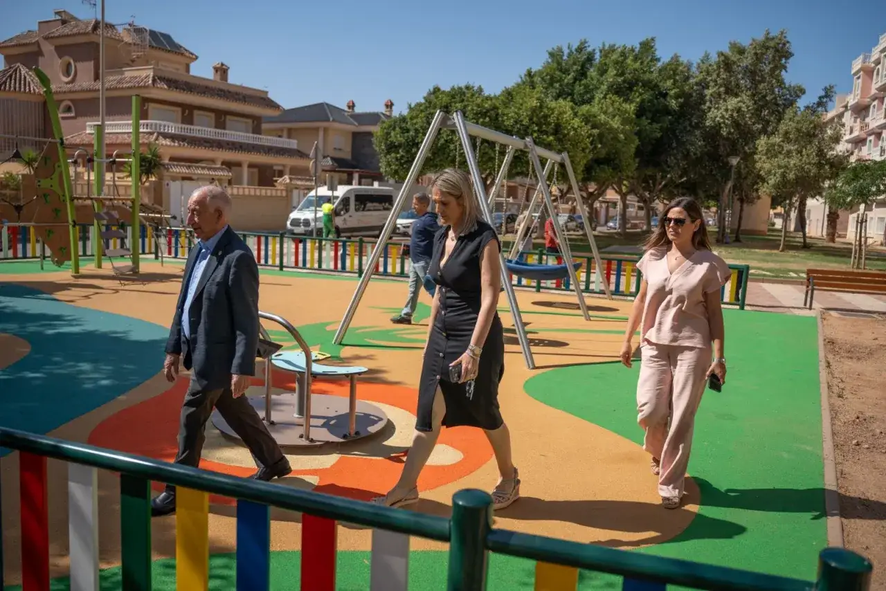Tres personas caminan por un colorido parque infantil en Roquetas de Mar. Hay columpios y estructuras de juego.