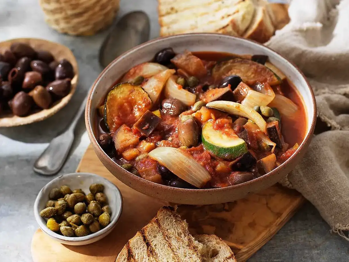 En sk&aring;l med siciliansk caponata, full av aubergine, zucchini, oliver och kapris. Serveras med rostat br&ouml;d.