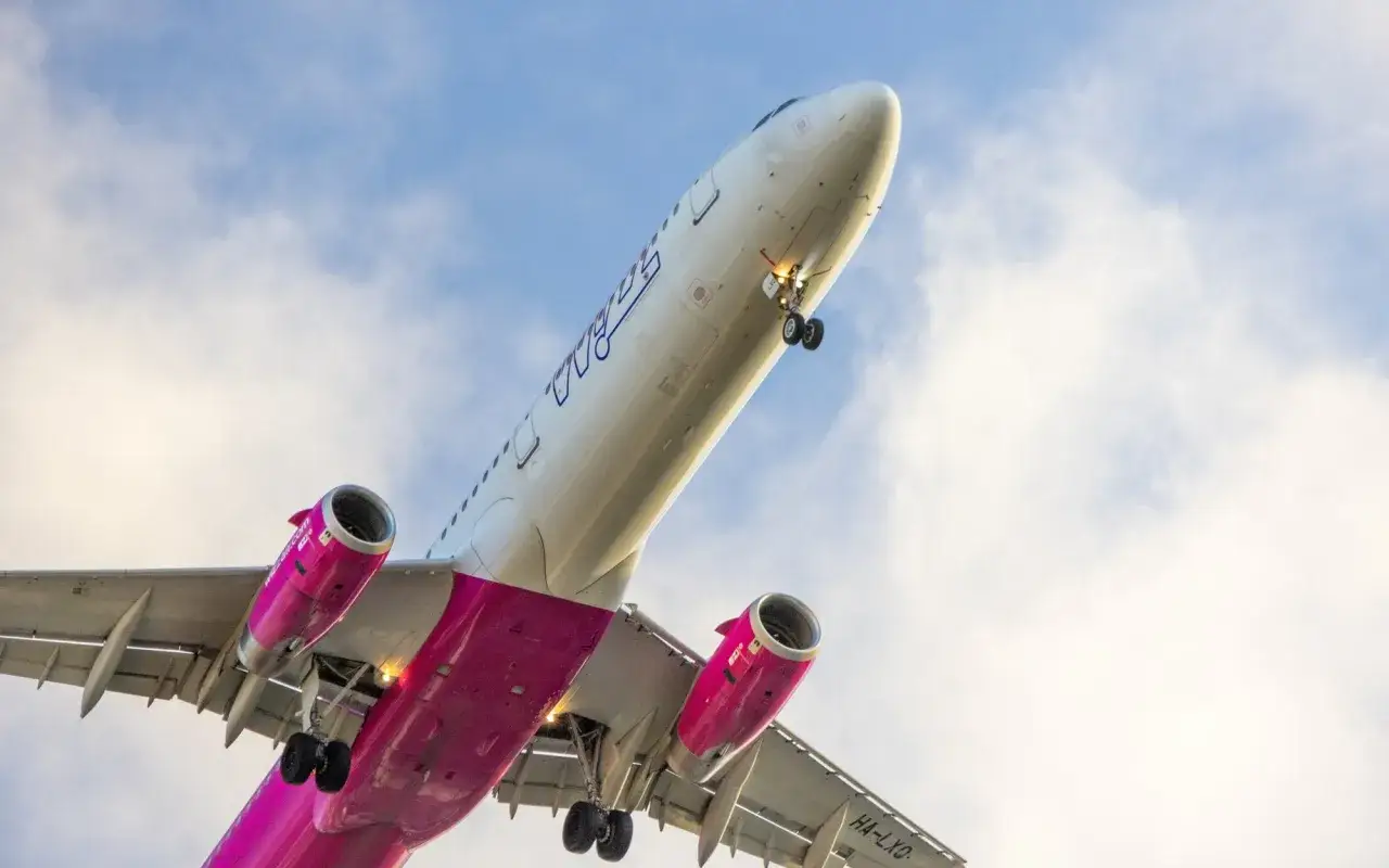 Samolot Wizzair, znane linie lotnicze, wznosi się na tle błękitnego nieba z chmurami.