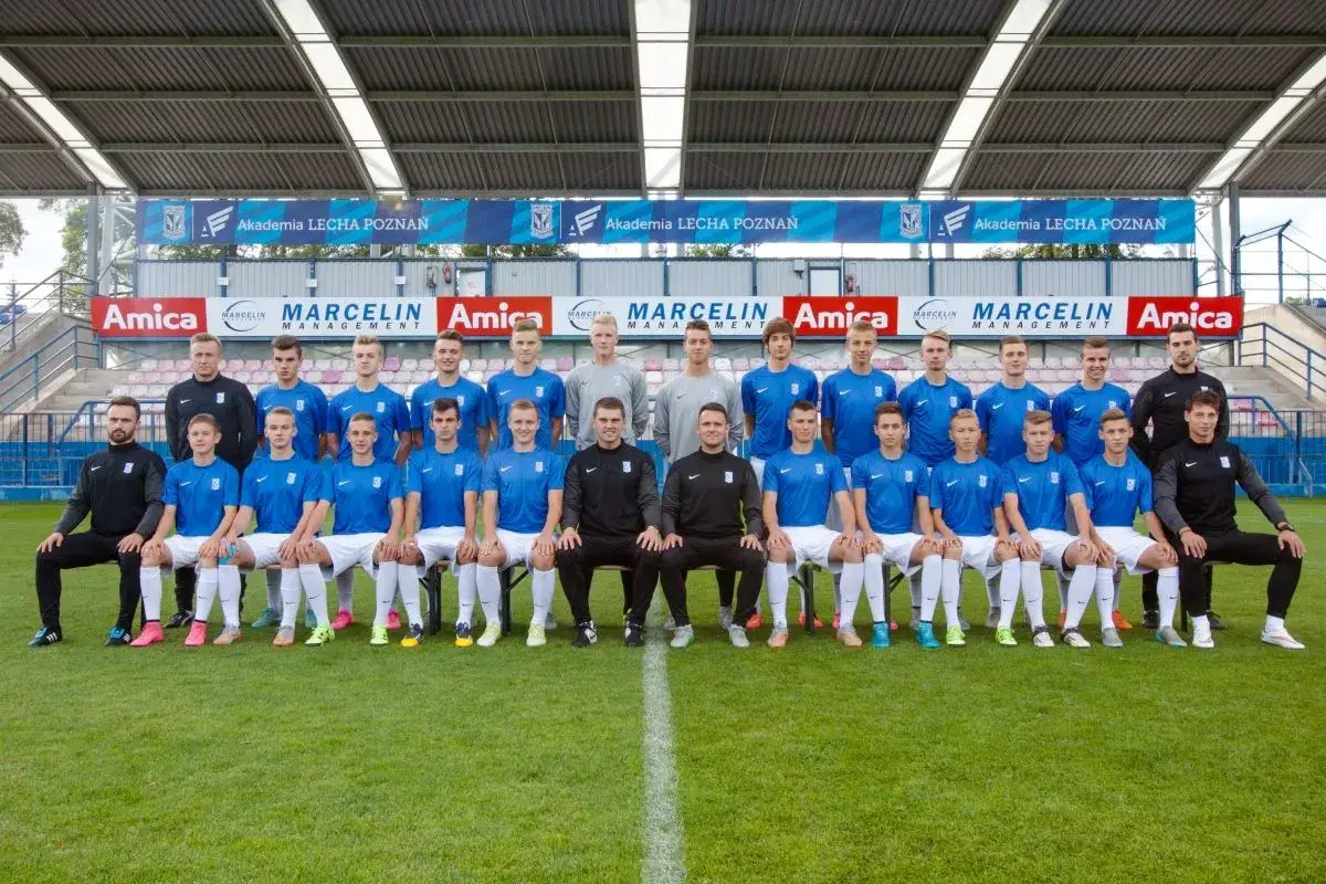 Młodzi wychowankowie Lecha Poznań w strojach klubowych pozują do zdjęcia na murawie.