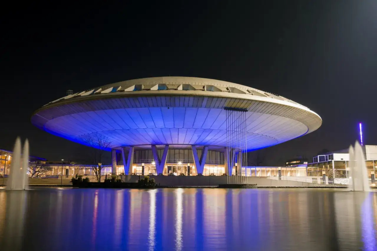 Nocne Eindhoven: futurystyczny budynek z niebieskim podświetleniem i fontannami, jedna z głównych atrakcji miasta.