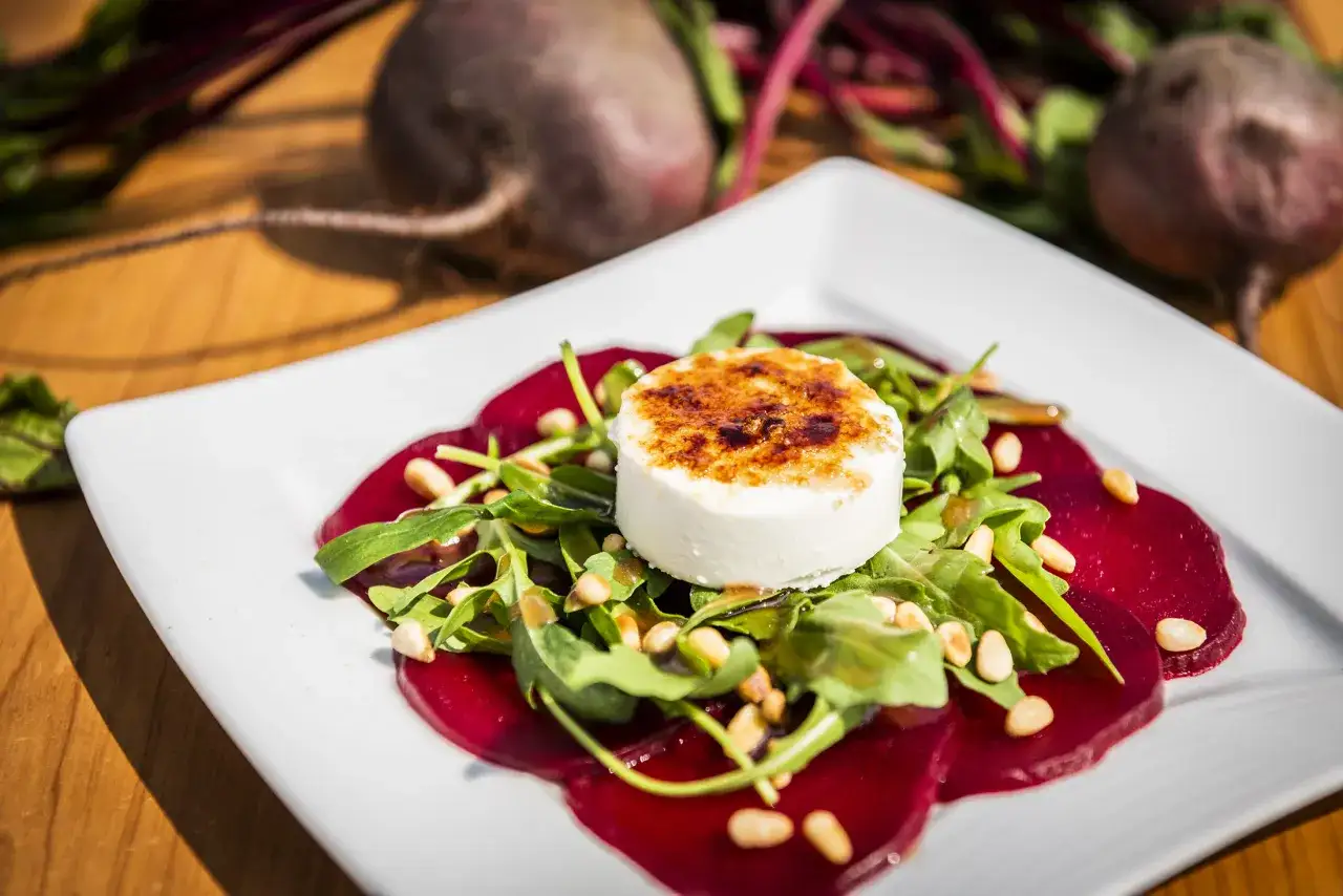 Rote Bete Carpaccio mit Ziegenkäse und Pinienkernen auf einem weißen Teller, garniert mit Rucola.