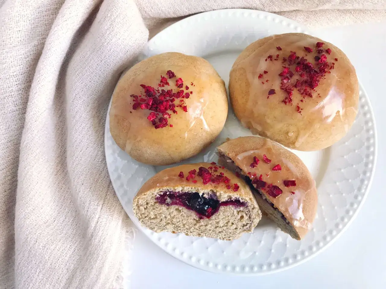 Trzy pączki z lukrem i malinami, jeden przekrojony, ukazujący jagodowe nadzienie. Idealne fit pączki na zdrowe śniadanie.