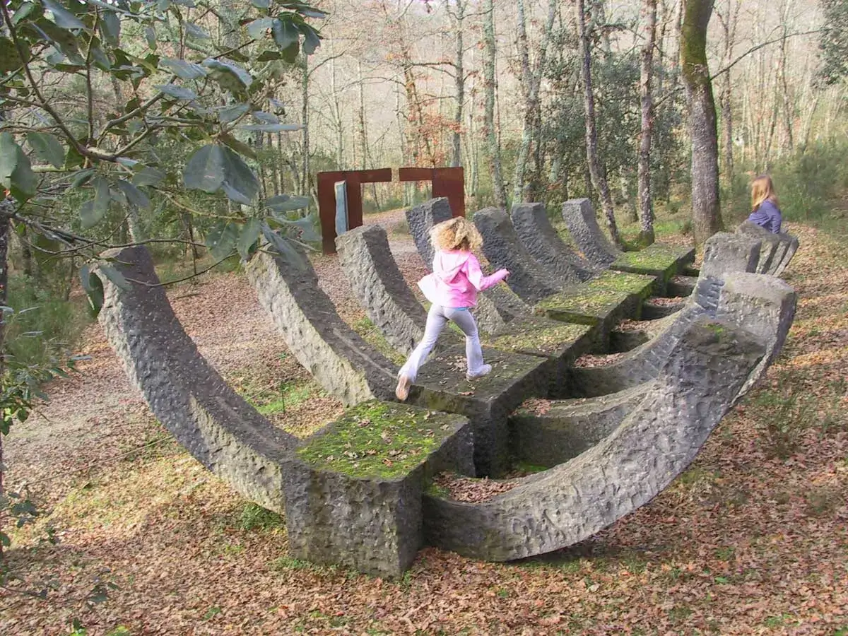 Bambina corre su una scultura in pietra nel **Chianti Sculpture Park**. Altre opere d'arte e alberi sullo sfondo.
