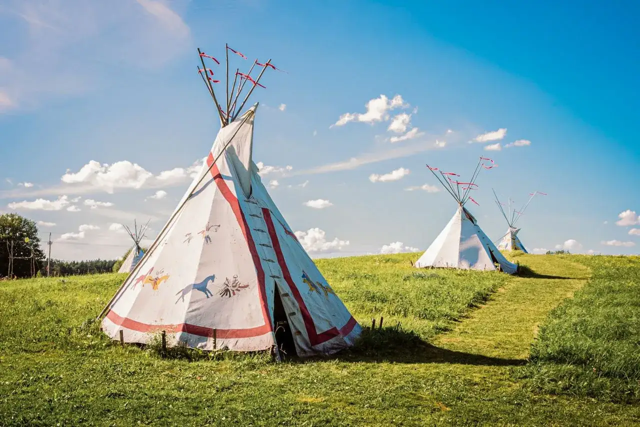Wioska indiańska na Mazurach. Białe tipi z malowidłami na tle błękitnego nieba z chmurami.