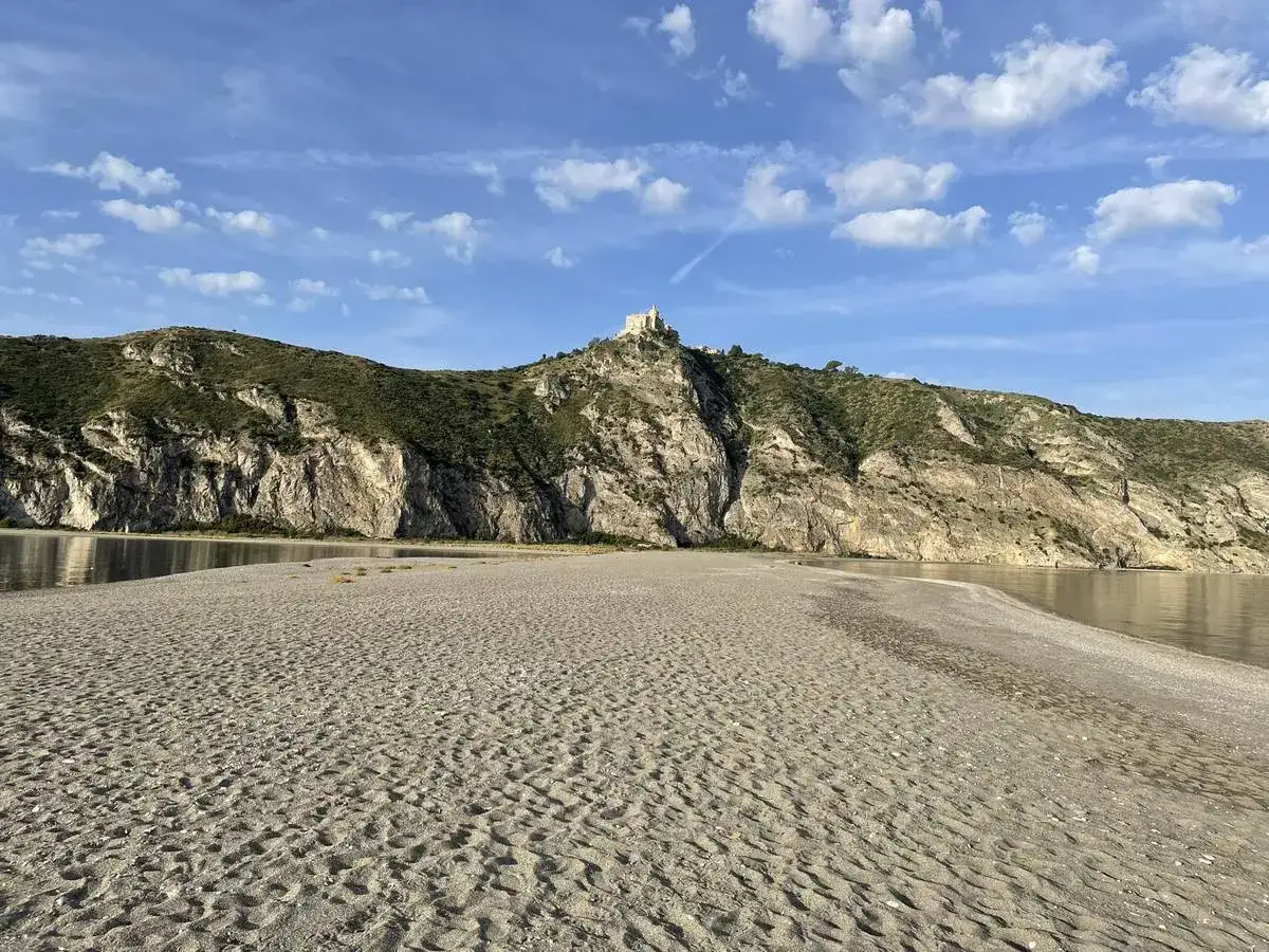 Plage de Patti, Sicile. Un château domine la colline rocheuse surplombant la mer calme et la plage de sable fin.