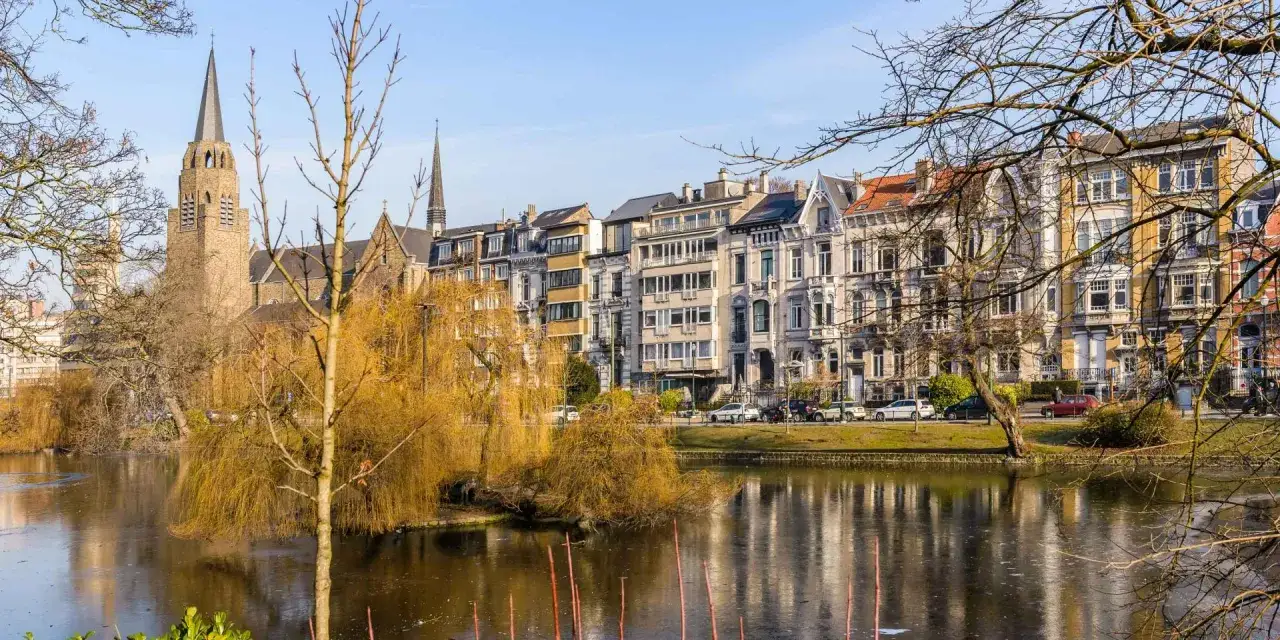 Vue d'un &eacute;tang gel&eacute; devant des maisons de ville et une &eacute;glise, un d&eacute;cor parfait pour visiter Bruxelles.