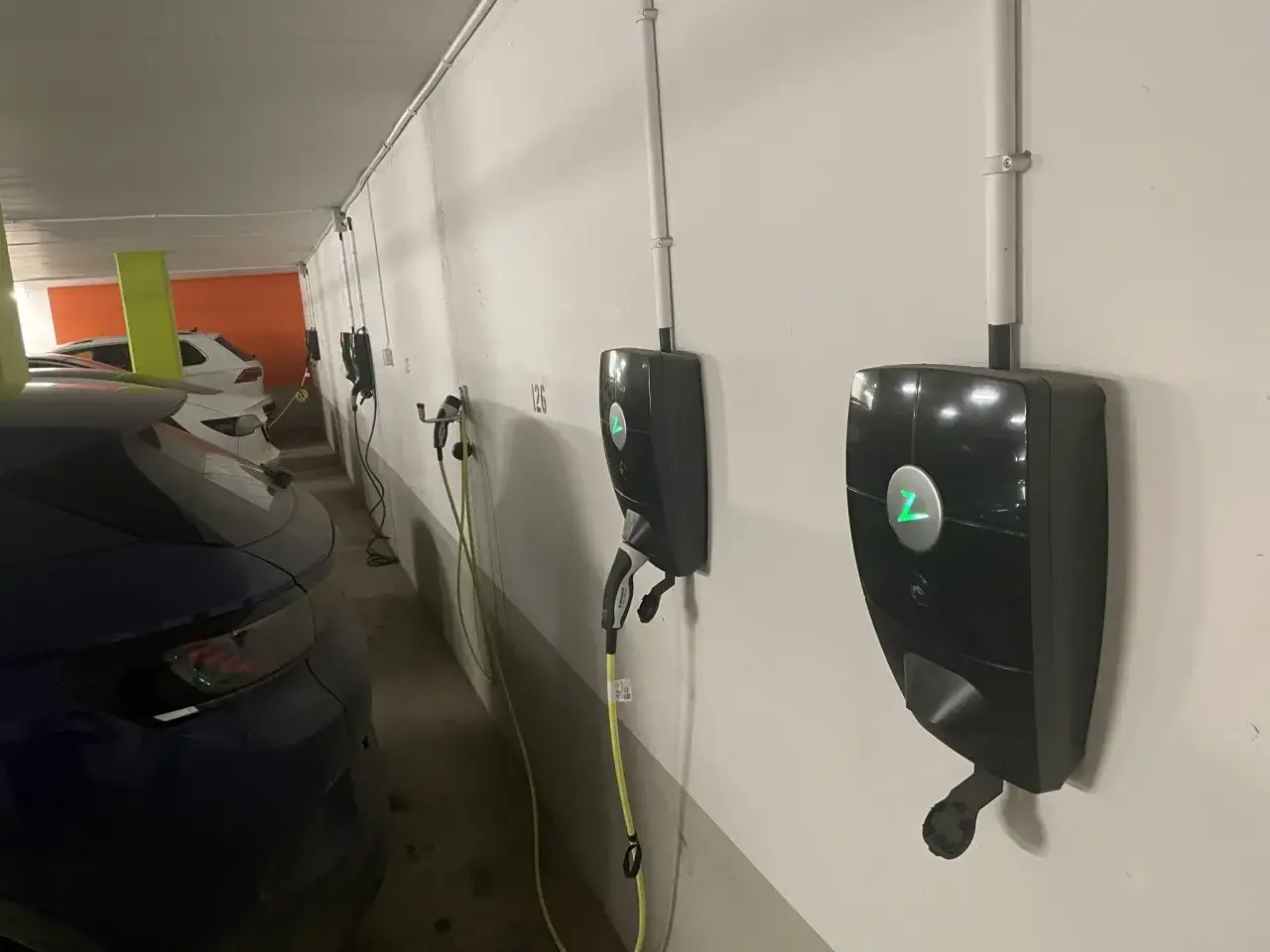 Flera laddstolpar för elbilar i ett garage. En blå elbil syns i förgrunden. Brf:en har satsat på bidrag för laddstolpar.