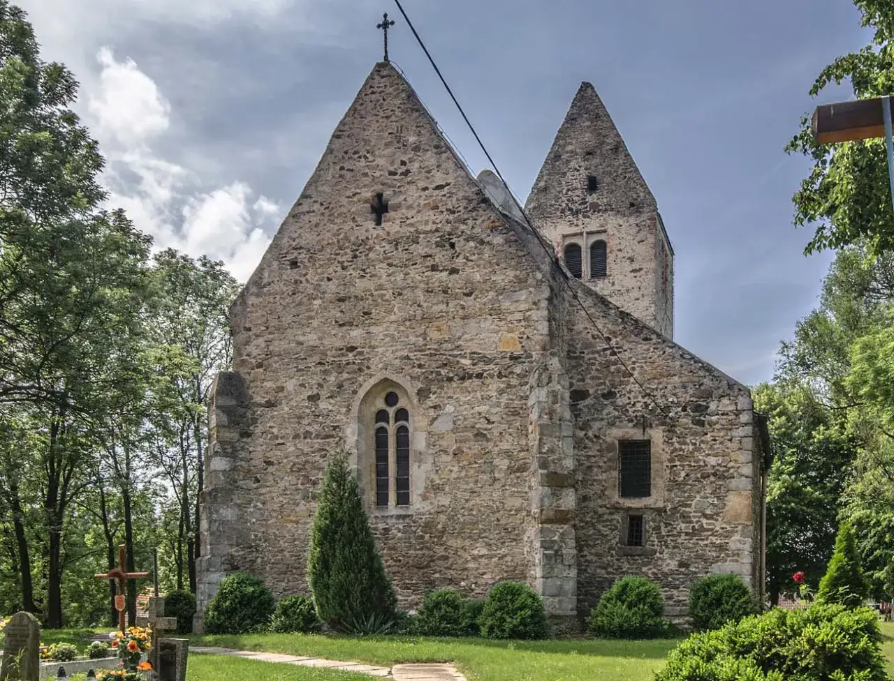 Kamienny kościół z wieżą, otoczony zielenią. To miejsce, gdzie średniowiecze najważniejsze informacje o architekturze i historii są wciąż żywe.