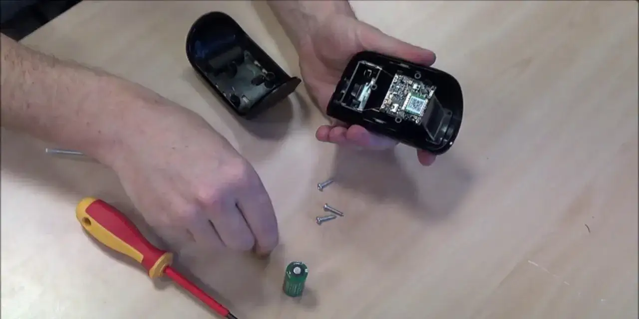 Démontage d'une alarme filaire pour vérifier la durée de vie batterie. Une pile et des vis sont visibles.