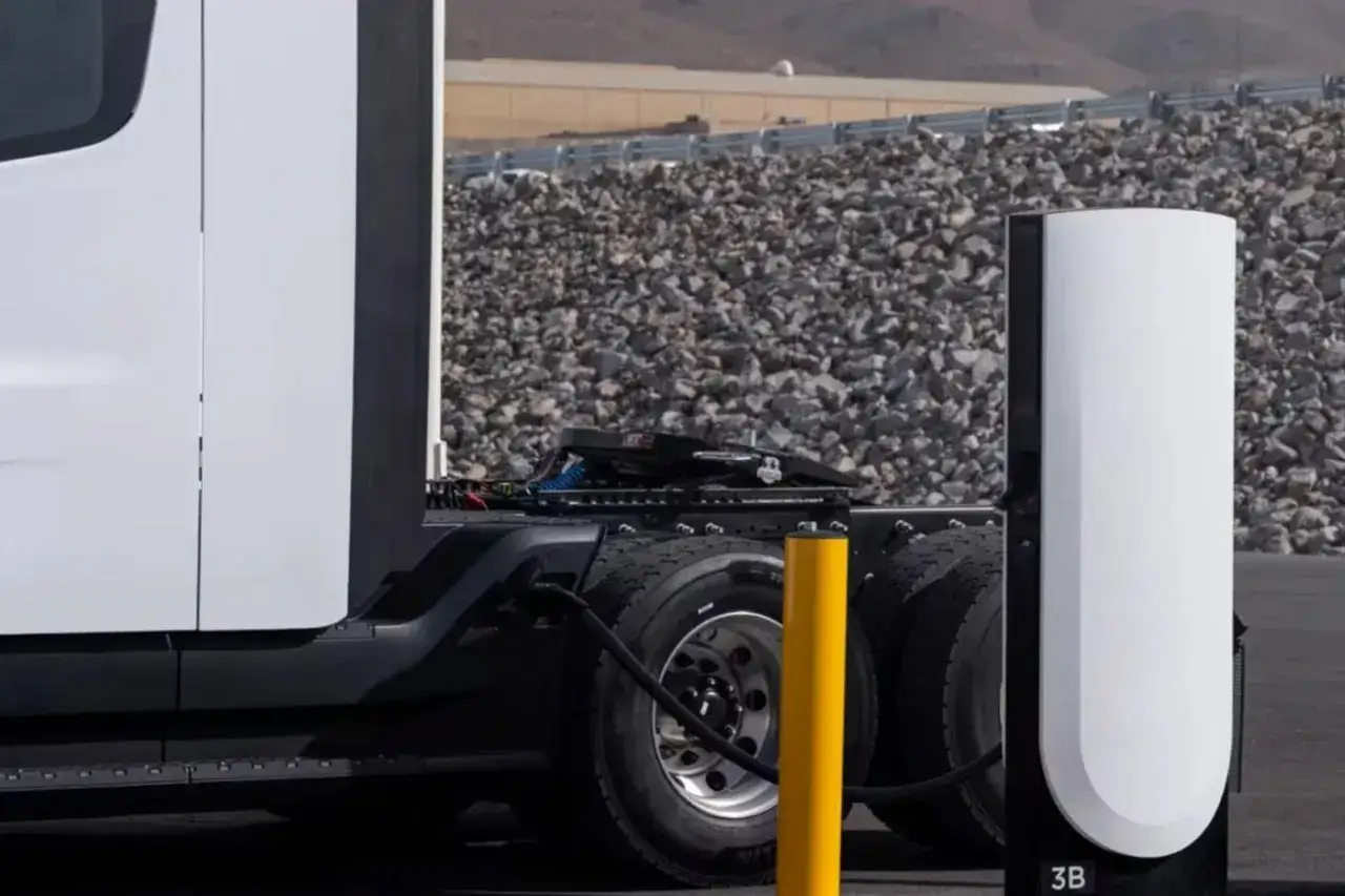 Biały Tesla truck podłączony do ładowarki. W tle kamienie i góry.