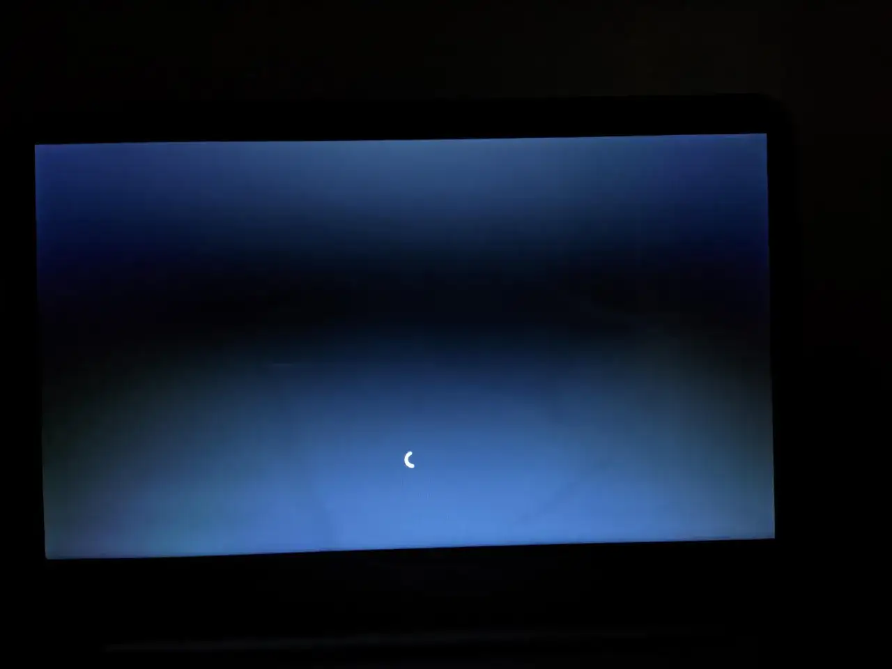 Ekran laptopa z niebieskim tłem i białym wskaźnikiem ładowania, sugerującym aktualizację oprogramowania.