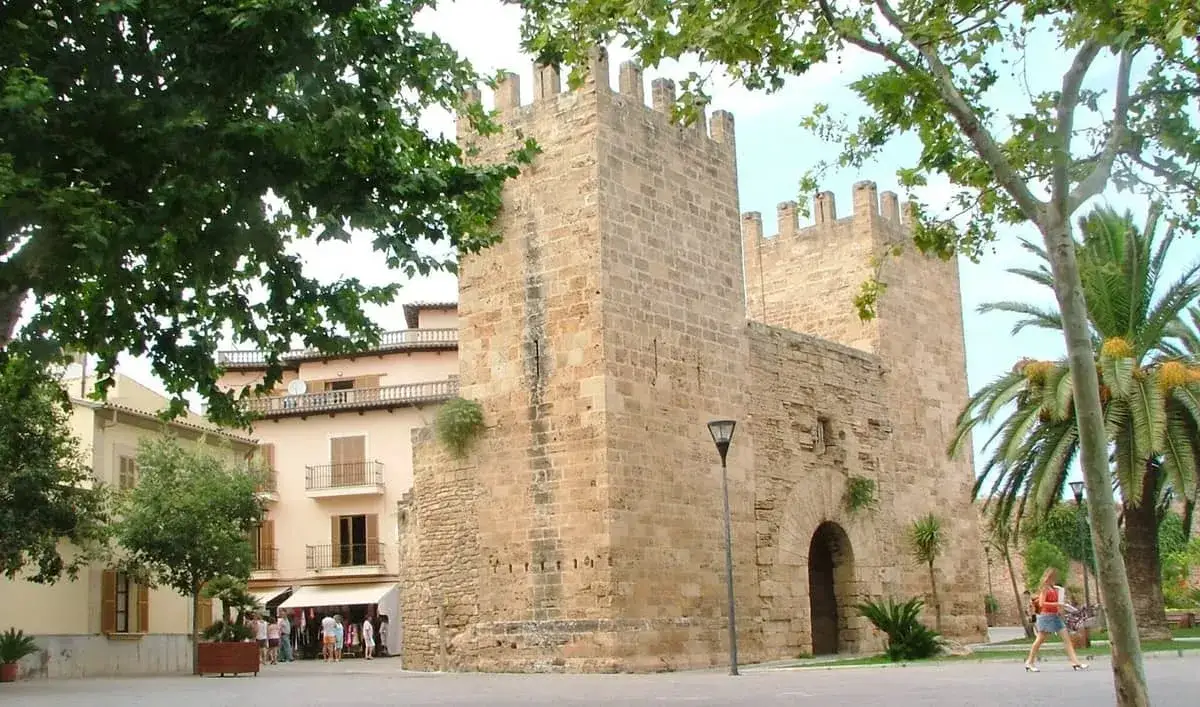 Kamienne mury Alcudia stare miasto, z łukowym wejściem i palmami w tle.