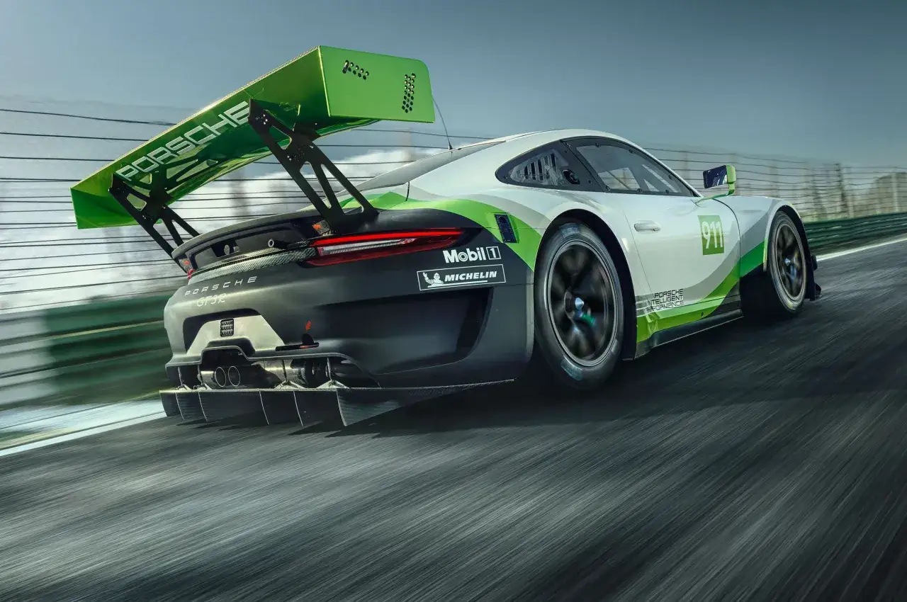 Wyścigowy Porsche 911 GT3 R pędzi po torze, jego zielone akcenty i ogromne skrzydło budzą podziw.