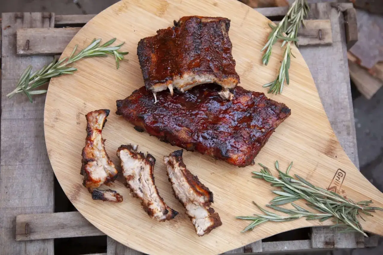 Saftige BBQ-Rippchen, bereit zum Genießen. 3, 2, 1... rippchen! Rosmarin garniert das Holzbrett.