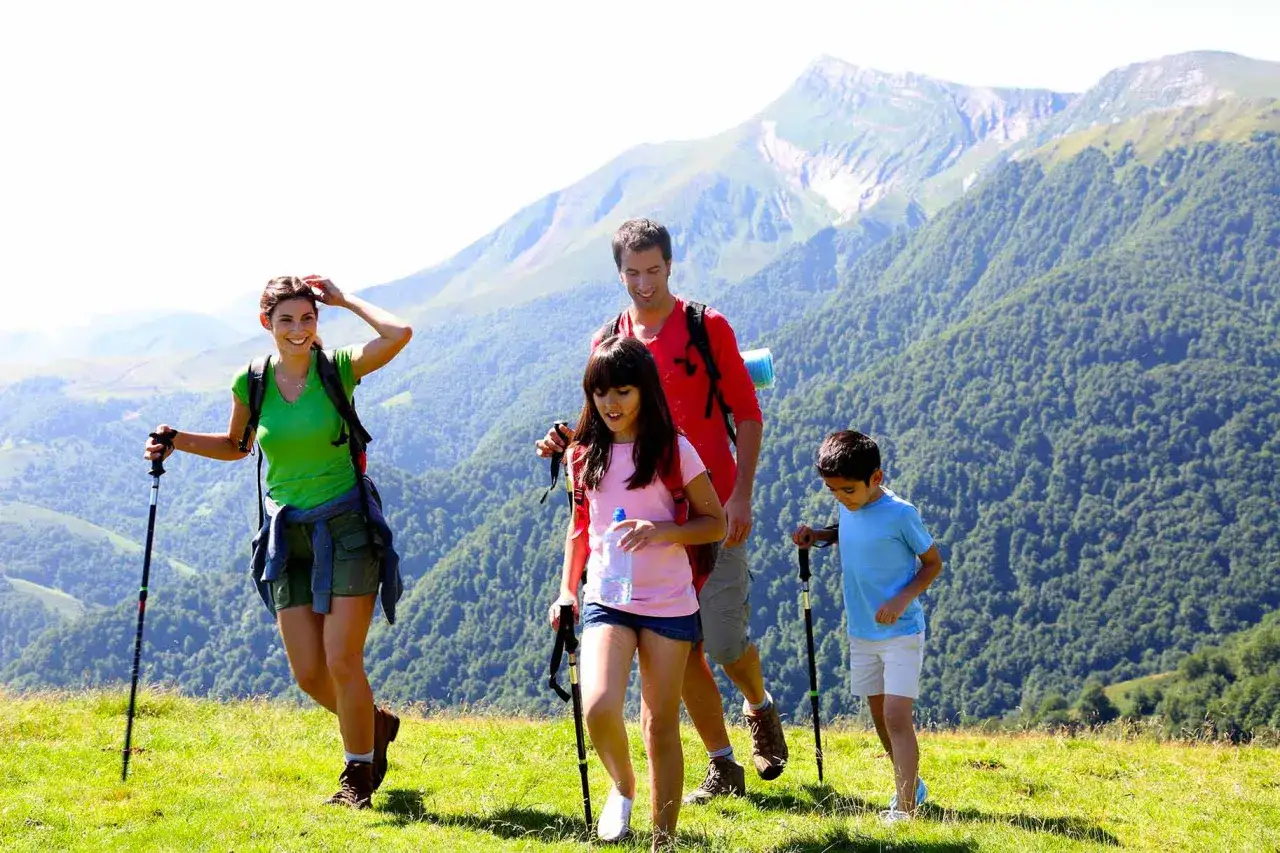 Famiglia in escursione in montagna, con bambini felici che si godono le vacanze in un paesaggio verdeggiante.