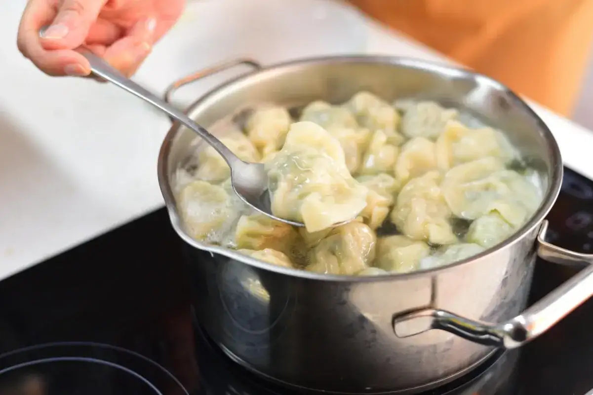 Gotujesz pierogi, które wcześniej zamroziłeś. Łyżka wyciąga jednego z garnka z wrzątkiem.