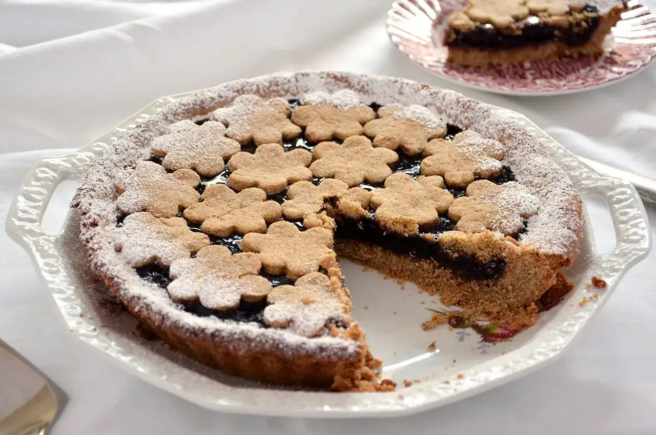 Deliziosa crostata di grano saraceno con marmellata scura e decorazioni a fiore, spolverata di zucchero a velo.