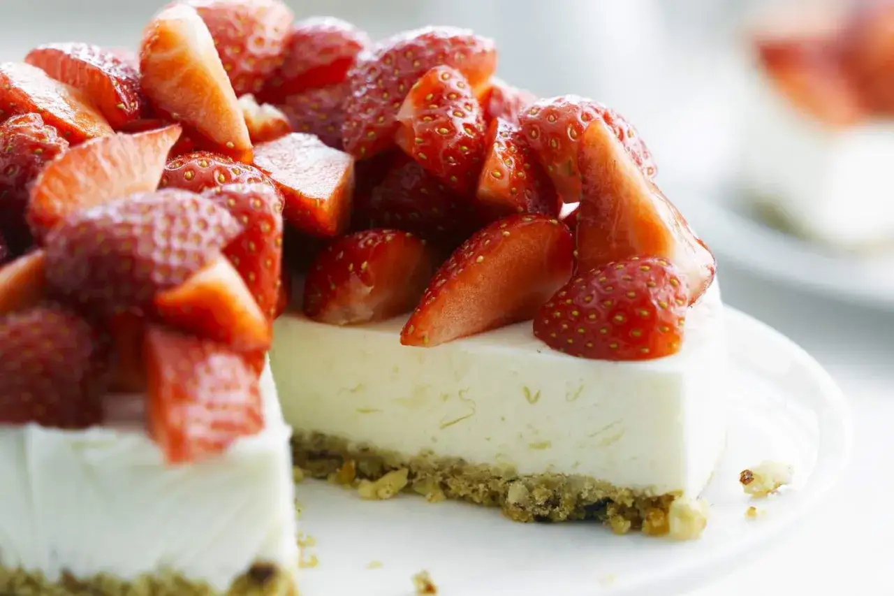 Tranche de cheesecake fraise, garnie de fraises fraîches coupées. Un délice fruité et crémeux.