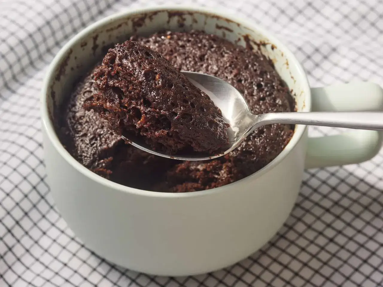 En sked lyfter en bit av en saftig chokladkaka ur en mugg. Perfekt för ett snabbt muggkaka recept.