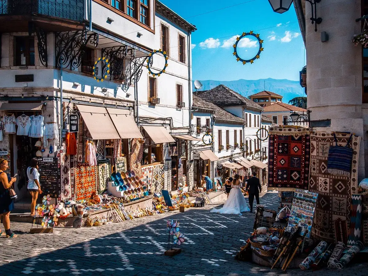 Ulica w Gjirokastrze, Albania, pełna kolorowych dywanów i pamiątek. Czy Albania jest droga? Zakupy tutaj wydają się przystępne.