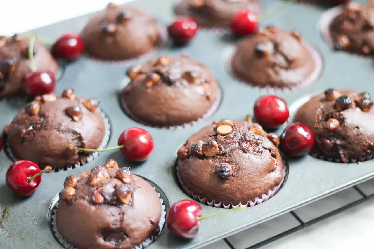 Schoko Kirsch Muffins in einer Muffin-Form, garniert mit frischen Kirschen und N&uuml;ssen.