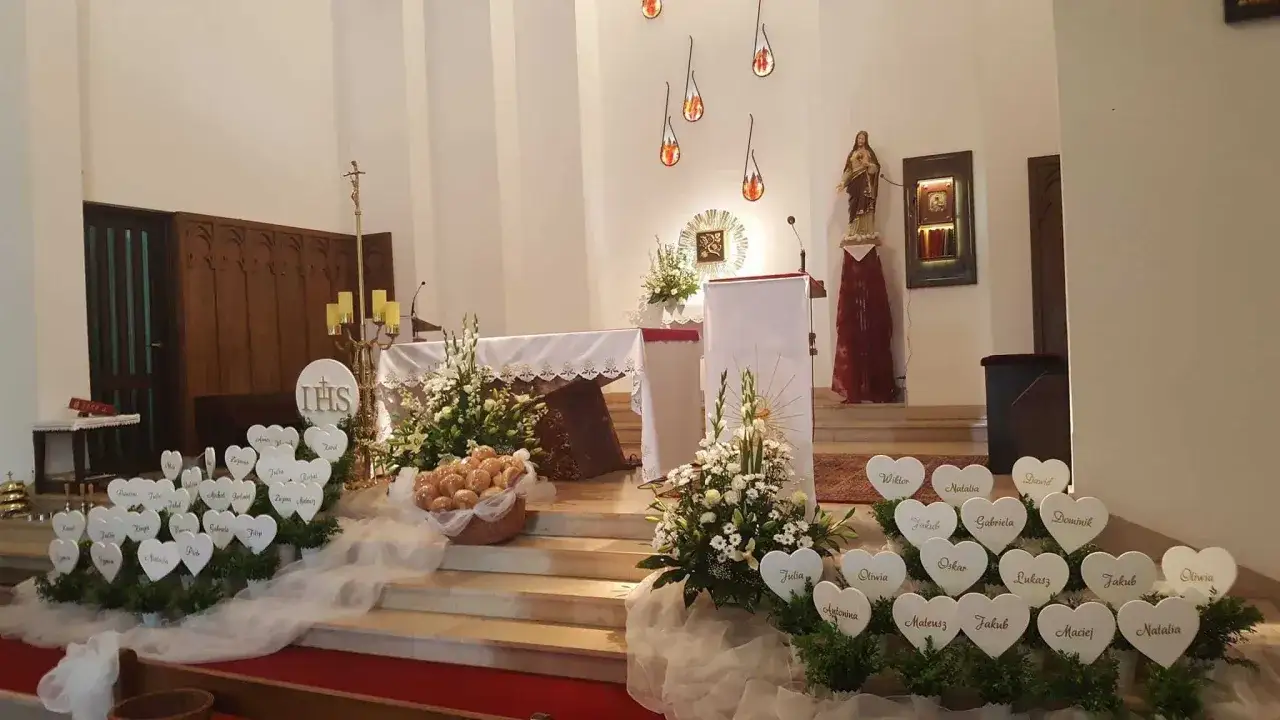 Serce z imionami dzieci, przygotowane na komunię bez spowiedzi. Ołtarz ozdobiony kwiatami i koszem z hostiami.