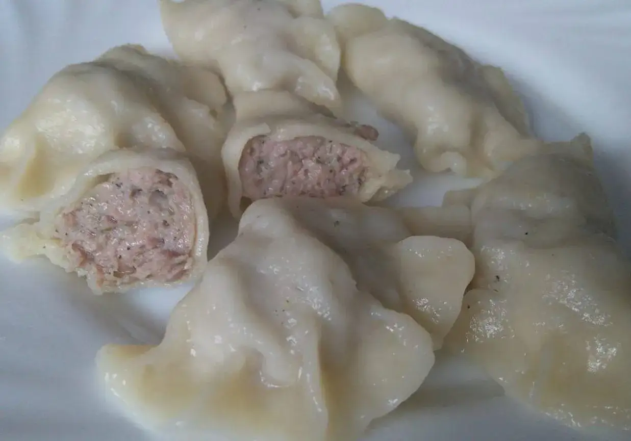 Pyszne pierogi z białą kiełbasą, jeden przekrojony, ukazujący soczyste nadzienie.