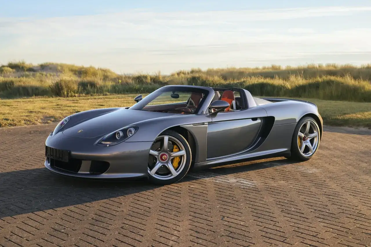 Szary Porsche Carrera GT z brązowym wnętrzem na tle wydm i nieba.