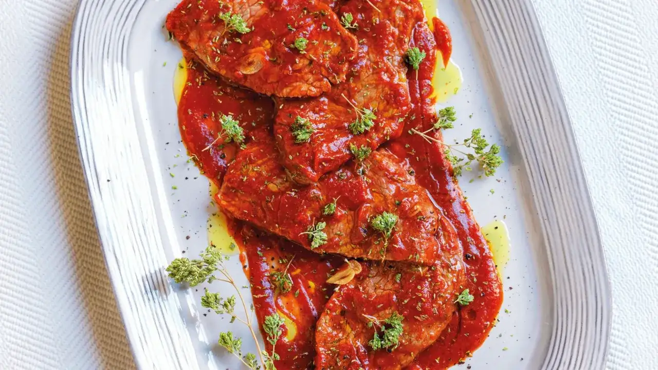 Bistecche alla pizzaiola con mozzarella, succulente fettine di manzo in salsa rossa, guarnite con erbe aromatiche fresche.