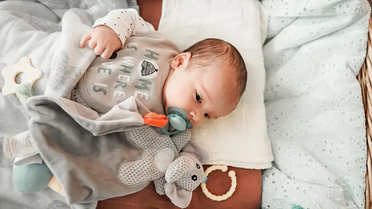 Noworodek z gryzakiem i smoczkiem w łóżeczku. Nawet w niespokojny sen, otulony miękkimi kocykami, czuje się bezpiecznie.