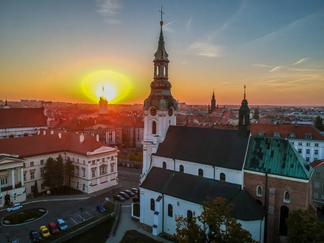 Zachód słońca nad Kaliszem tworzy magiczną atmosferę, idealną dla romantycznych miejsc. Widok na kościół i zabytkowe kamienice zapiera dech w piersiach.