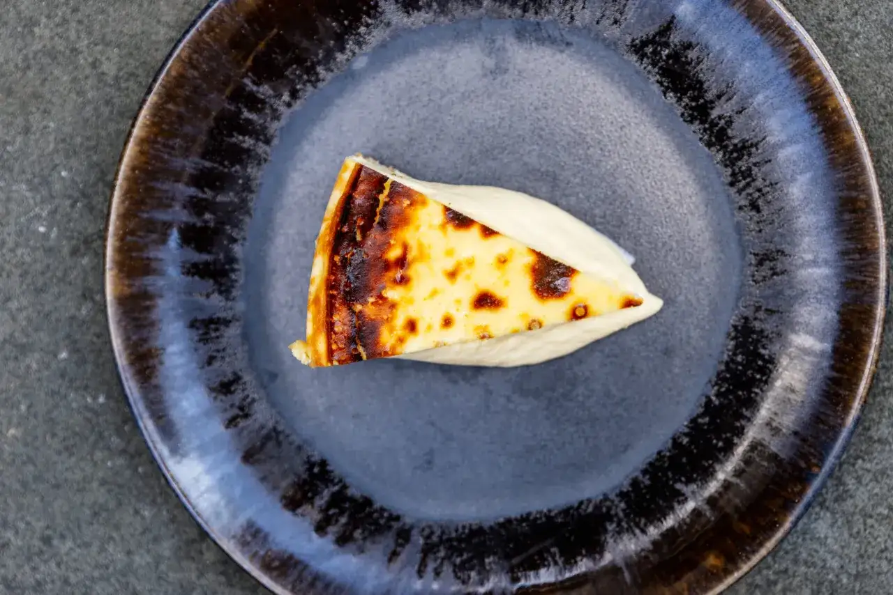 Ein Stück cremiger San Sebastian Cheesecake mit karamellisierter Kruste auf einem dunklen Teller.