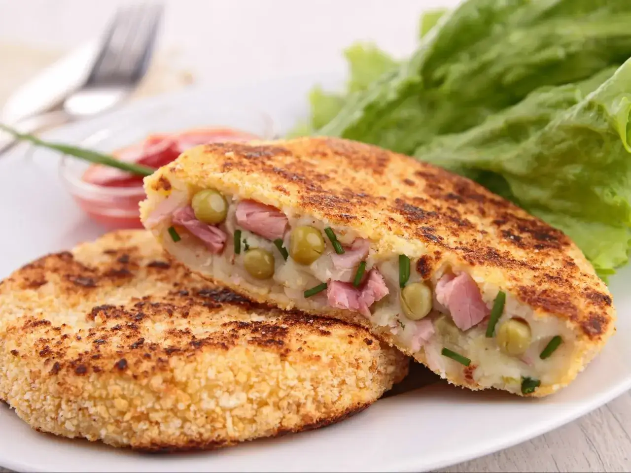 Placuszki z ziemniaków z szynką i groszkiem to świetny pomysł, co zrobić z ugotowanych ziemniaków. Podane z sałatą i sosem.
