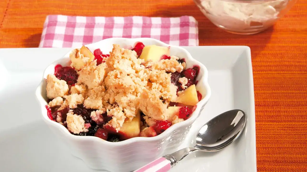 Ein köstliches Beeren-Apfel-Crumble-Rezept in einer weißen Schale, garniert mit knuspriger Streuseldecke.