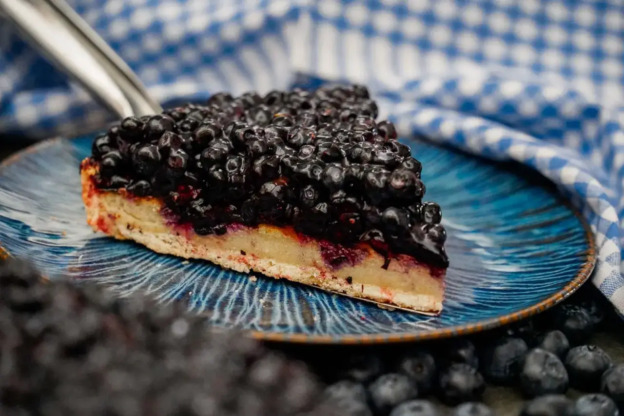 Une part généreuse de tarte myrtille Savoie, garnie de fruits frais et juteux, sur une assiette bleue ornée.