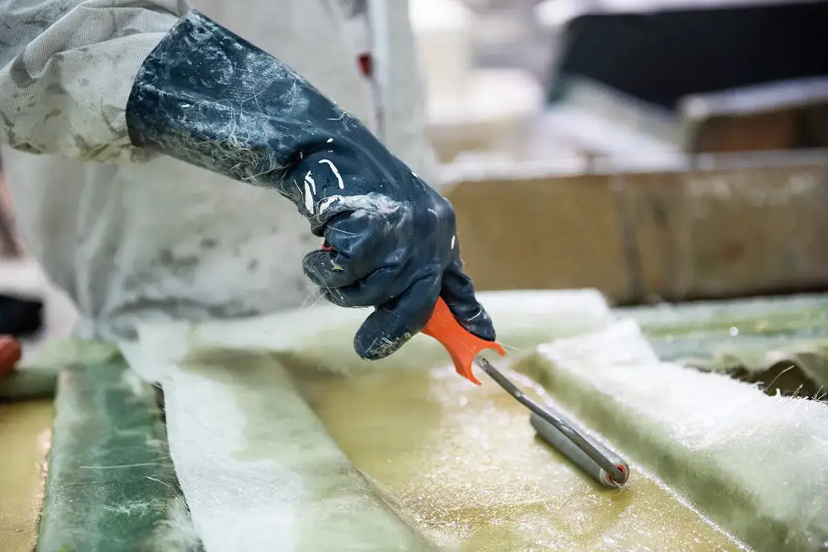 Arbetare med gummihandske rullar ut glasfiber f&ouml;r att laga en b&aring;t.