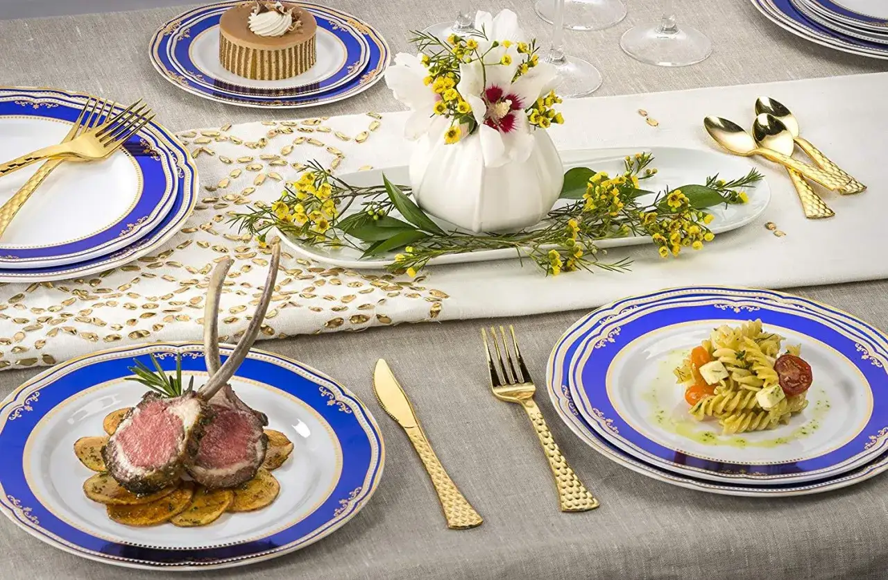Un couvert de table &eacute;l&eacute;gant avec des assiettes bleues et dor&eacute;es, des couverts dor&eacute;s, un gigot d'agneau et un petit g&acirc;teau.
