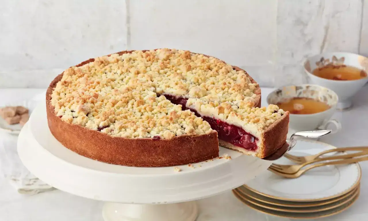 Ein saftiger Kirschkuchen mit Streuseln, perfekt für Ihr nächstes kirschkuchen rezept. Serviert mit Tee und goldenem Besteck.