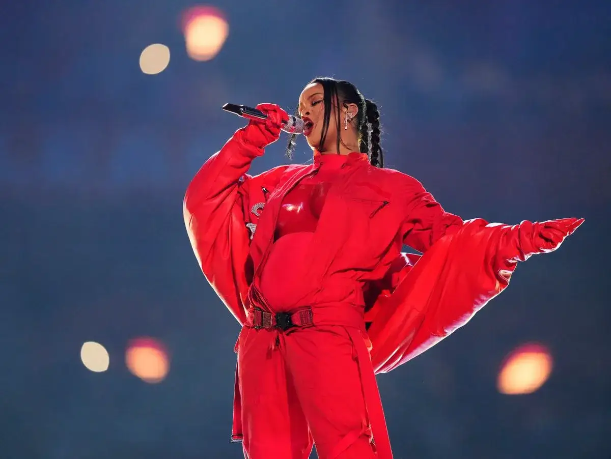Rihanna singt in einem roten Outfit, das ihren Babybauch betont. Fans hoffen auf ein neues Lied von ihr.