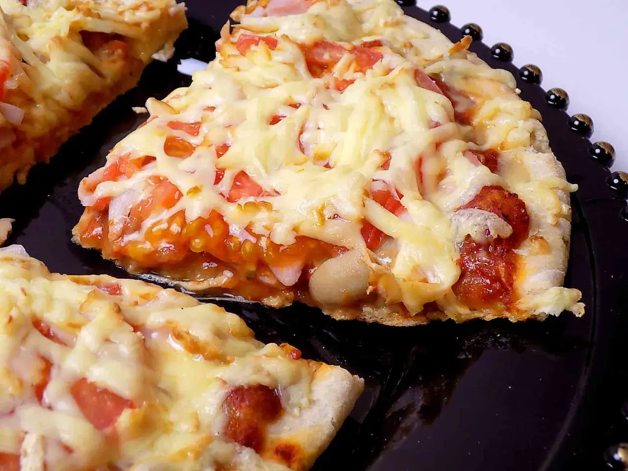 Pyszna pizza z patelni z ciągnącym serem, pomidorami i kawałkami kiełbasy na czarnym talerzu.