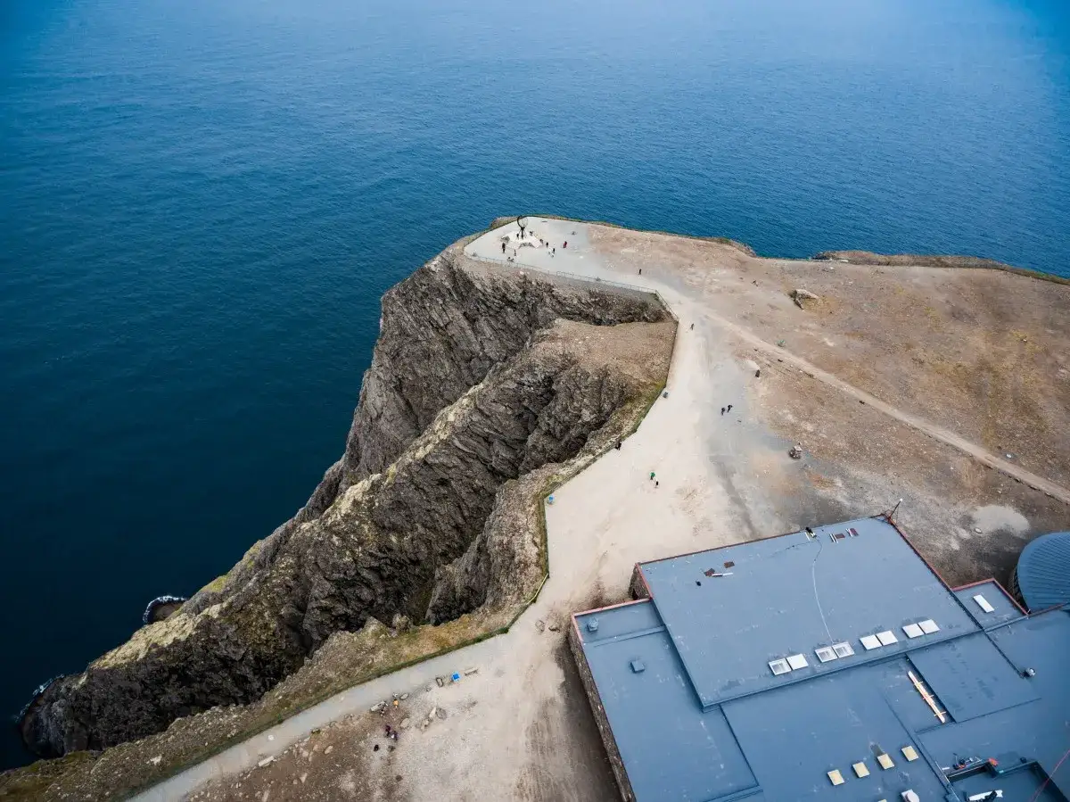 Widok z lotu ptaka na klifowe wybrzeże i budynek turystyczny na Nordkapp. Turyści podziwiają ocean.