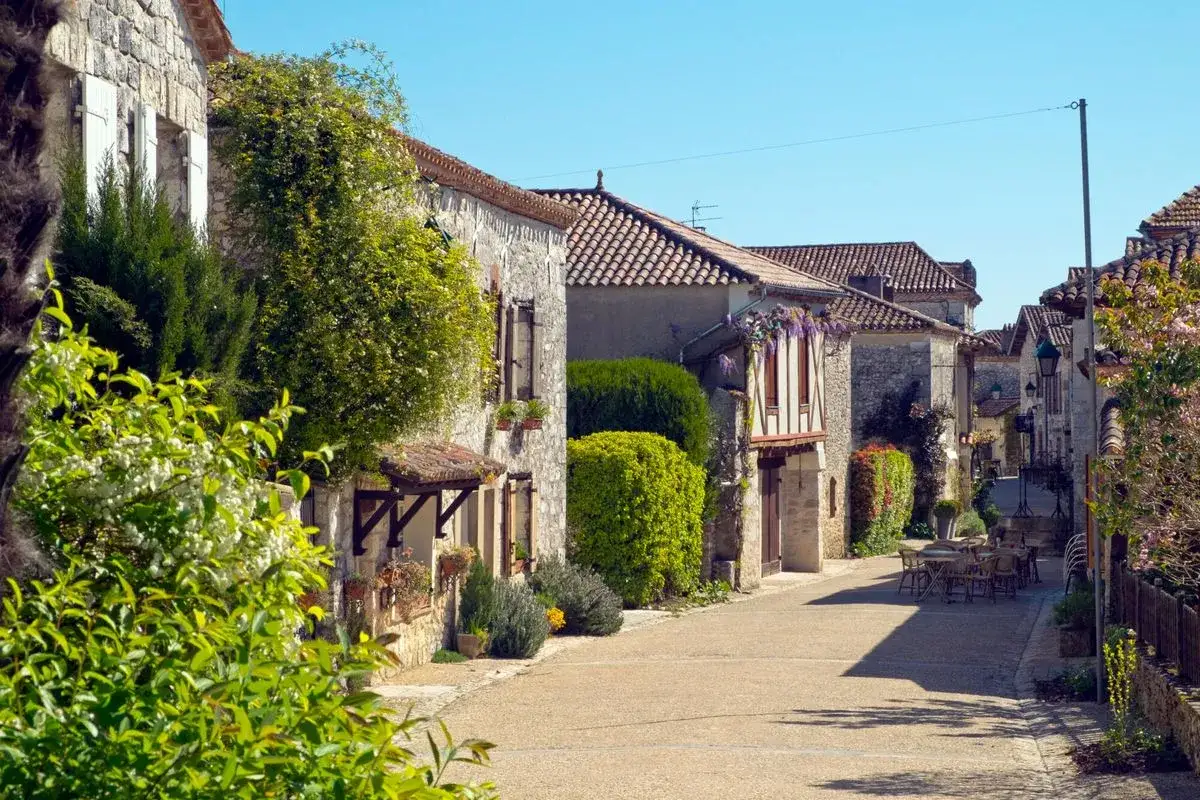 Rue pavée bordée de maisons en pierre et de végétation luxuriante, typique du circuit des plus beaux villages du Lot.
