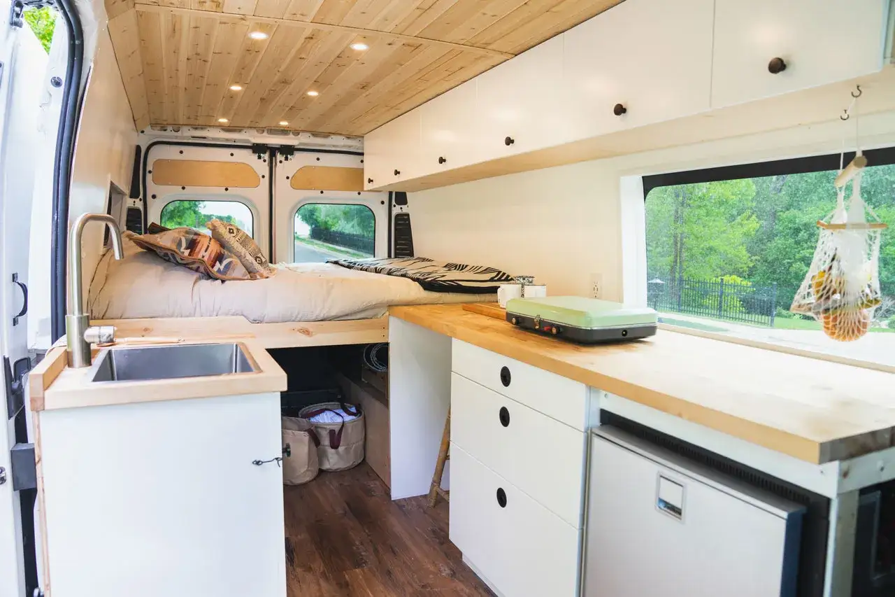 Int&eacute;rieur d'un petit fourgon am&eacute;nag&eacute; : lit douillet, &eacute;vier, cuisine compacte et rangements. Parfait pour l'aventure !