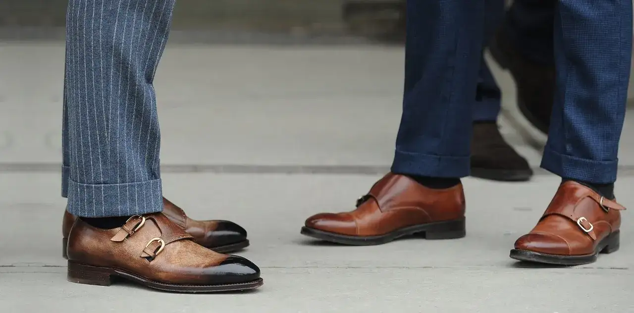 Eleganckie buty i idealna długość spodni garniturowych. Dwa mężczyzn w stylowych, brązowych butach i granatowych spodniach.