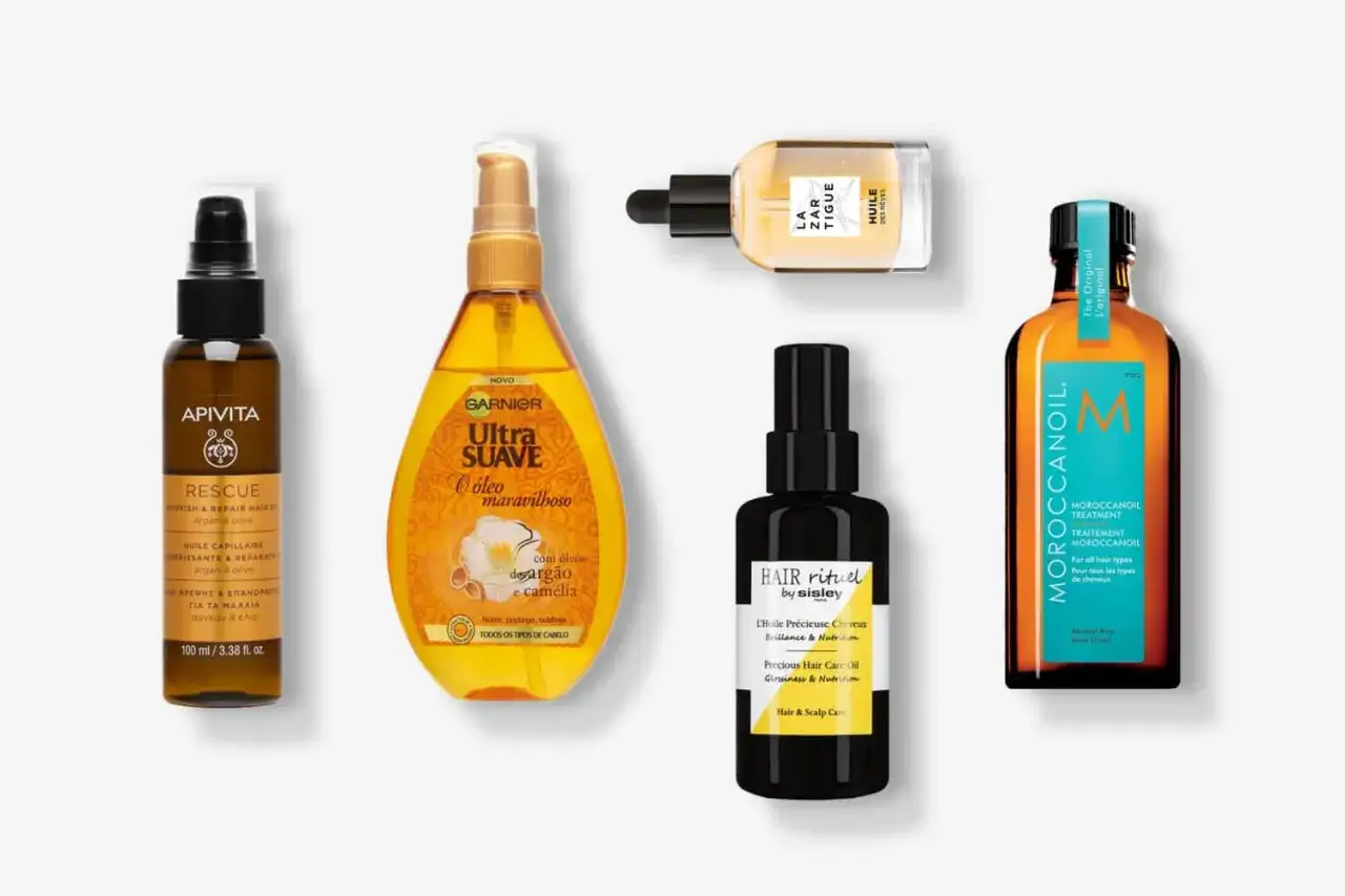 Flera flaskor med olja i håret, inklusive märken som Apivita, Garnier, Sisley och Moroccanoil, arrangerade på en vit bakgrund.